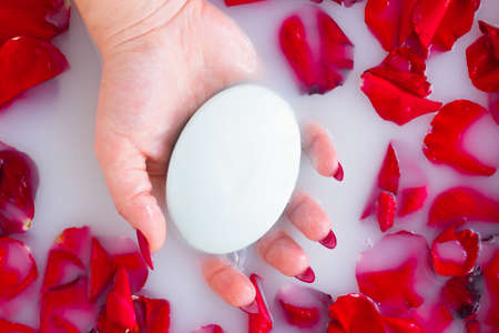 Female hand hold soap against the background of milk or white water with rose petalsの写真素材