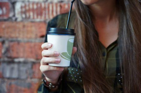 girl holding a disposable coffee cup on a background of a brick wall