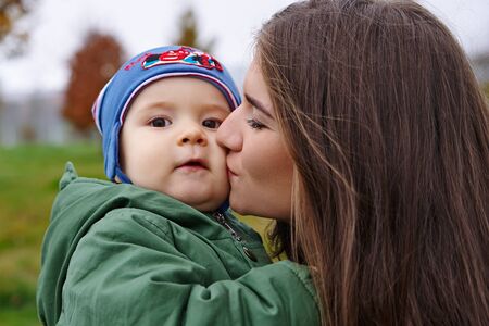 Happy kid mum on his hands in the park in autumn.の写真素材
