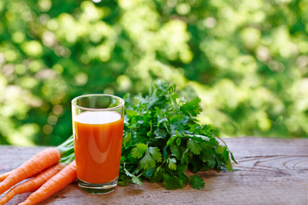Carrot juice in a glass and fresh carrots on a rustic wooden tableの写真素材