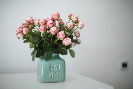 Beautiful pastel pink roses in a shabby chic crackled vase with the word happiness on it.の写真素材