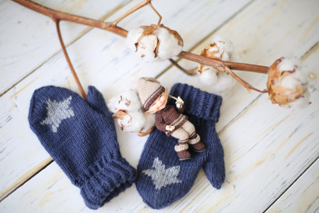 Knitted cosy mittens with real cotton on the white rustic wooden background.