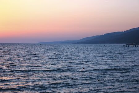 Sunset on mountainous seashore in bay with boats and pier.の写真素材