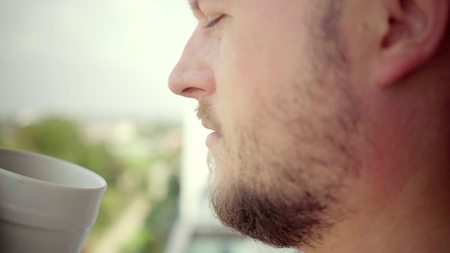 man on the balcony drinking with a white mug, close-up. Blank drink cup for your design. Can put text, imageの写真素材