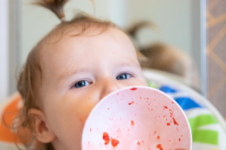 Attractive baby eats strawberries from a white plate and is all smeared with. Fresh berriesの写真素材