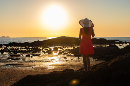 girl in a hat strolls along the beach at sunset.の写真素材