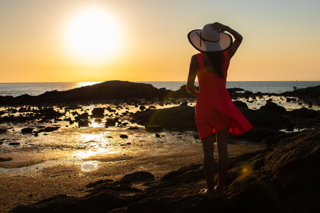 girl in a hat strolls along the beach at sunset.の写真素材