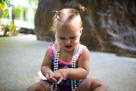 a girl in a bathing suit with white beads is surprised, rejoices, shouts, raises her hands. childrens fashion conceptの写真素材