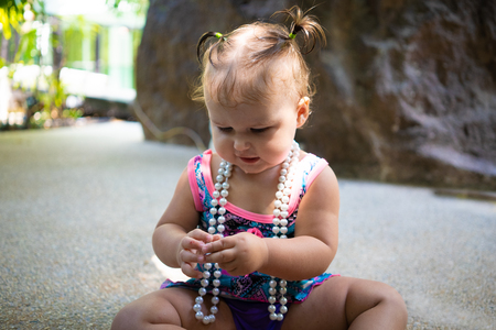 a girl in a bathing suit with white beads is surprised, rejoices, shouts, raises her hands. childrens fashion conceptの写真素材