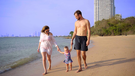 Happy family at the beach, holding hands, waving a little girl around. Mom dad daughter walk on the beach.の写真素材