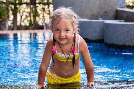 little girl in a yellow swimsuit in a blue pool like a mermaid. kids concept, kids fashionの写真素材