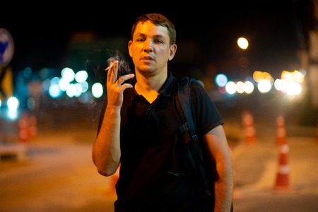 man smoking a cigarette on the street at nightの写真素材