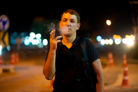man smoking a cigarette on the street at nightの写真素材