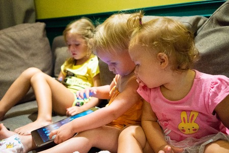 three little girls are looking into smartphones and tablets. the problem of dependence of children on gadgetsの写真素材