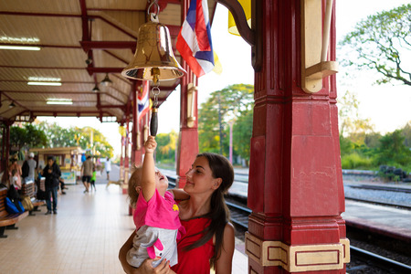 mother holds daughter in her arms, girl and child beat the bell at the station in Huahin Thailandの写真素材