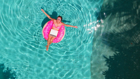 Aerial view of a young brunette woman swimming on an inflatable big donut with a laptop in a...