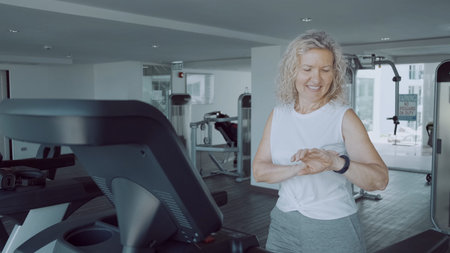 senior woman doing sports on a treadmill in the gym using a sports cardio watch.