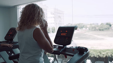 senior woman is engaged on a treadmill in the gym. female chats on the phone doing the treadmill.