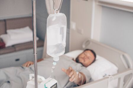 Male lying on a hospital bed. Dropper in a mans hand in a hospitalの写真素材