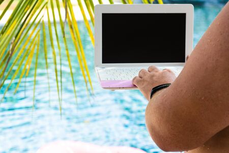 Male working on his laptop, sitting by the pool. Male hands on the keyboard in the pool.の写真素材