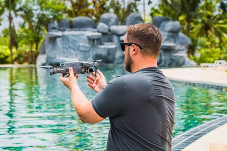 A sympathetic man launches a drone for flight, with which you can take photos and videos, near the swimming pool, view backの写真素材