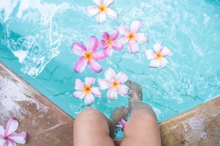 Baby feet in a swimming pool. Tropical flowers Frangipani Plumeria, Leelawadee floating in the water. Spa pool. Peace and tranquility. Spa conceptの写真素材