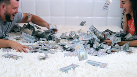 Female and male throw at each other a lot of banknotes of dollars on the bed, slow motion, top view.