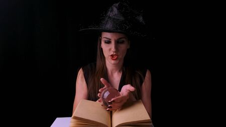 woman in a black witch costume and hat, holds a transparent magic ball in her hands and conjures. Halloween holiday partyの写真素材