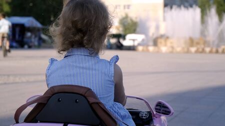 little girl in a blue dress rides a pink baby car in a park. Happy childhood concept. Caricature of an adult woman driving a carの写真素材