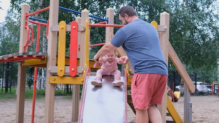 Dad and daughter play in the playground, a man catches a daughter who moves down from a childrens slideの写真素材