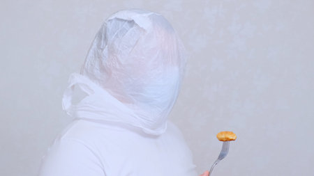 bearded man in a bag on his head and a protective mask has a cutlet from a fork. Fear of...