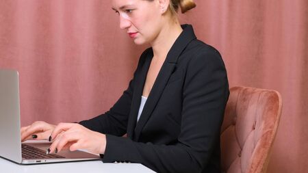 Woman is using laptop while sitting at her desk. Young european businesswoman is sitting in the office and working on notebook softwareの写真素材