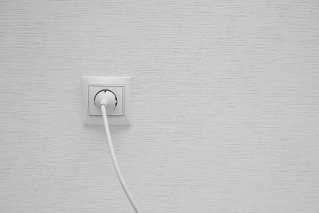 White electrical plug in the electric socket on a wall