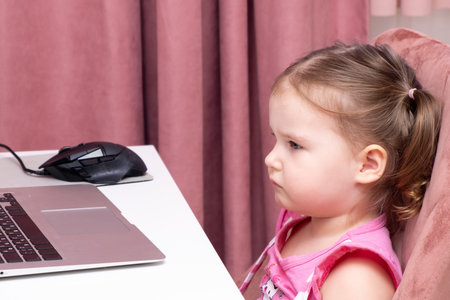 Beautiful cute sad little girl at a laptop. The concept of online learning with a laptop, distance...