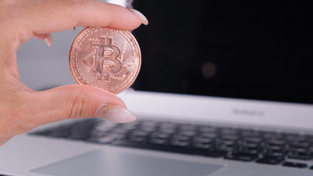 female hand holds Golden Cryptocurrency bitcoin with Notebook. Blurry of a Laptop and Cyrptocurrency...