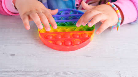 baby female hands playing with pop up sensory toy circle form. little female presses colorful rainbow squishy soft silicone bubbles on white background. Stress and anxiety relief. Trendy fidgeting gameの写真素材