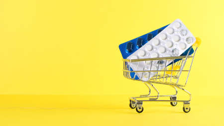 Shopping cart with pills on a yellow background, closeup. Medicine concept, online shopping.の写真素材
