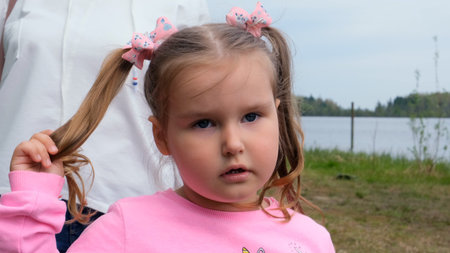 Portrait of a cute 3 year old girl, dressed in a pink sweatshirt with two ponytails, playing...
