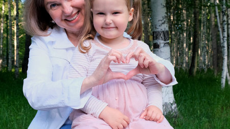 Happy loving grandmother and granddaughter, 3 years old, show their heart out of their hands. The...