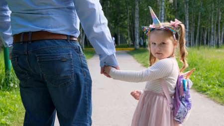 Cheerful Dad and daughter 3-4 years old go and hold hands on a walk in the park. Dad day. Happy childhood concept. back view.の写真素材