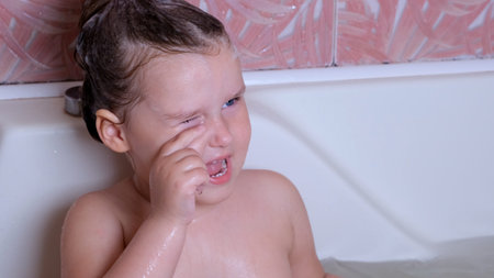 Little girl 3 years old bathes and washes in the bathroom at home, water gets into the eyes of the...