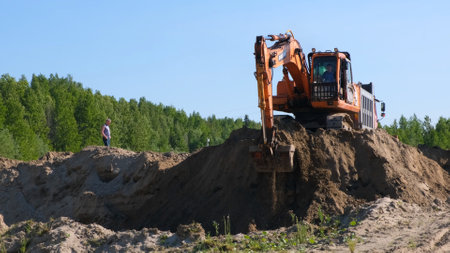 Yellow excavator bulldozer carries out earthworks by digging sand at a construction site: Moscow, Russia - August 30, 2021のeditorial素材
