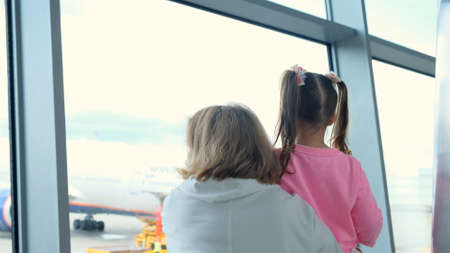 happy Mother and little girl at the airport in anticipation of landing look out the glass window at the planes. The concept of safe travel and flightsの写真素材