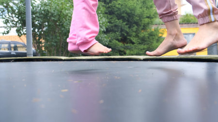 young woman and a young girl are jumping on a ram, close-up. Legs float in the air after jumping on a trampoline. Family fun, entertainment and sports, selective focus.の写真素材