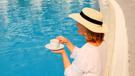 The culture of drinking tea and coffee. Woman with straw hat drinking hot drink from a cup near blue...