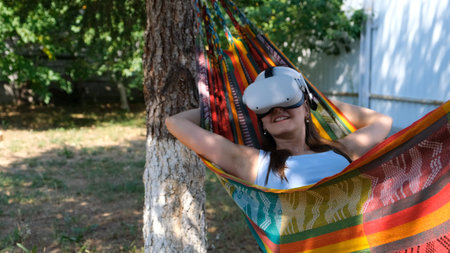joyful woman wearing virtual reality glasses rests in a hammock near a tree, imagining a dream come...