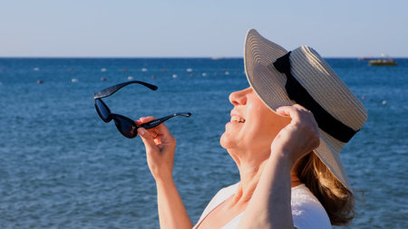 happy 50 year old woman in straw hat and sunglasses enjoying the sun against the blue sea...