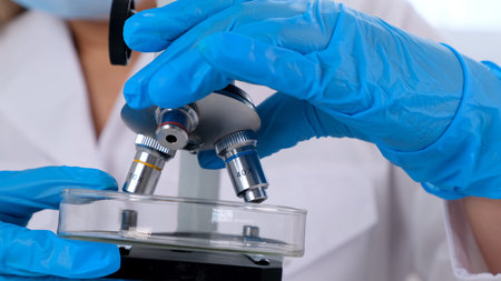 Hands of a researcher laboratory assistant in protective gloves holding a microscope in the...