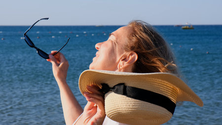 beautiful 50 year old woman in a straw hat and sunglasses on a blue sea background. Summer,...