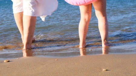 Grandmother and granddaughter walk along the coast and splash in the sea with their feet on a hot summer sunny day. The concept of summer holidays, fun, family.の写真素材